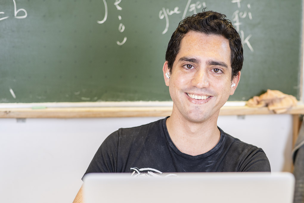 Ein Nachhilfelehrer mit Kopfhörern sitzt vor einer Tafel am Laptop