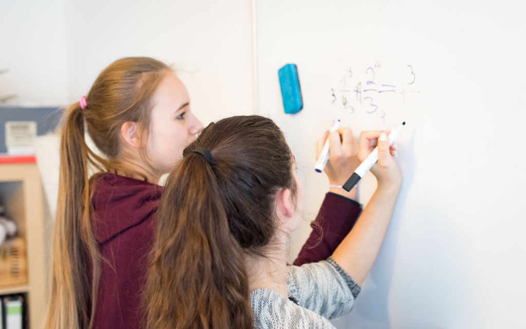 Zwei Schülerinnen rechnen gemeinsam eine Bruchaufgabe an einem Whiteboard