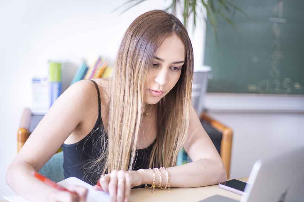 Eine Schülerin macht sich Notizen neben ihrem Laptop